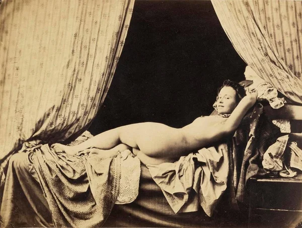 female-nude-with-courtains-over-dressed-bed-with-arms-around-head female